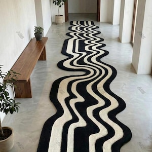 Könnte beinhalten: Ein langer, wellenförmiger Teppich mit einem schwarz-weißen Streifenmuster. Der Teppich liegt in einem Flur mit einer Holzbank und Topfpflanzen. Das Design erzeugt einen fließenden visuellen Effekt.