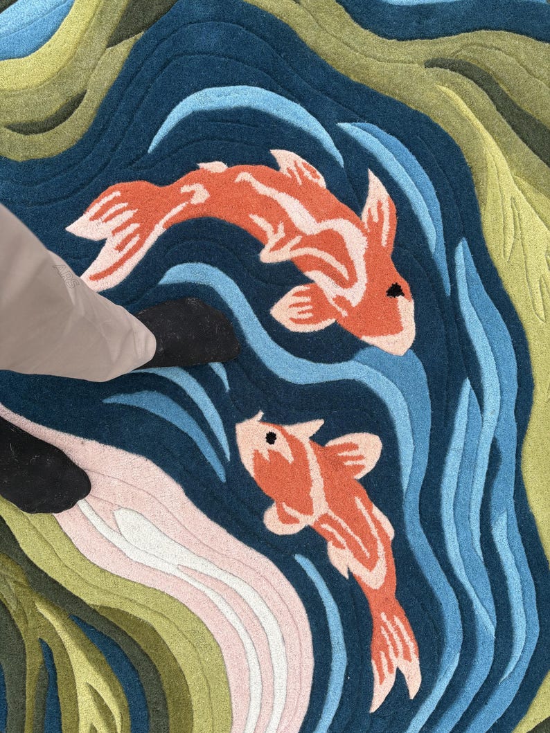 May include: A colorful rug featuring a koi pond design. Two orange and white koi fish swim in a blue pond with wave patterns. The rug has green, pink, and blue sections, creating a vibrant aquatic scene.