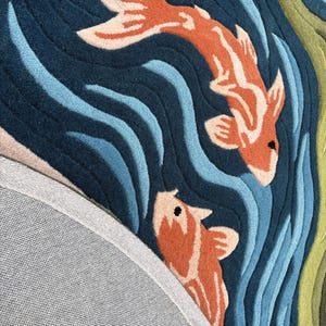 May include: A detailed rug featuring two orange and white koi fish swimming in a blue and teal water pattern. The rug has a dark blue background with wavy lines, and a gray backing is visible.