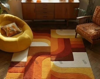 May include: A retro-style area rug with a geometric pattern in shades of orange, yellow, and brown. The rug features curved lines and rectangular shapes, creating a vibrant and textured design. The rug is placed on a wooden floor, complementing the warm tones.