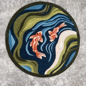 Handmade round hand-tufted New Zealand wool rug featuring two orange koi fish swimming through flowing blue water with green organic patterns in a Japanese Zen-inspired design.