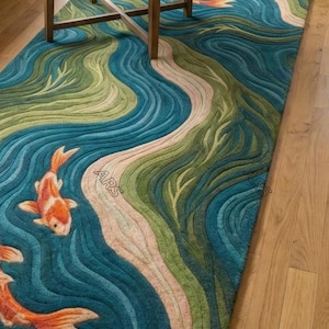 May include: A rectangular area rug with a koi fish design. The rug features a blue, green, and beige water pattern with orange and white koi fish. The rug is placed on a hardwood floor, with a wooden table in the background.