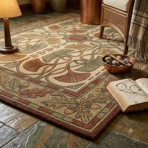 May include: A rectangular area rug featuring a cream background with a repeating pattern of green and brown ginkgo leaves and a border decorated with oak leaves and acorns. The rug is placed on a stone floor with a lamp, a bowl of stones, and a book.