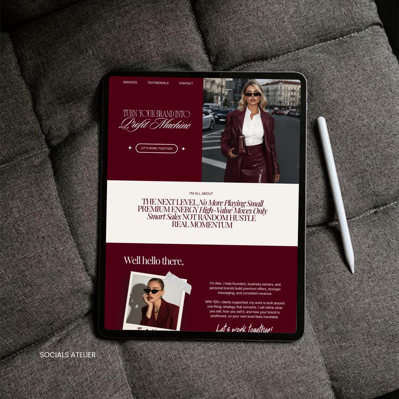 May include: A digital tablet displaying a website with a burgundy and white color scheme. The website's headline reads "Turn Your Brand Into Profit Machine." A white stylus rests beside the tablet on a gray fabric surface. The website features a photo of a woman.
