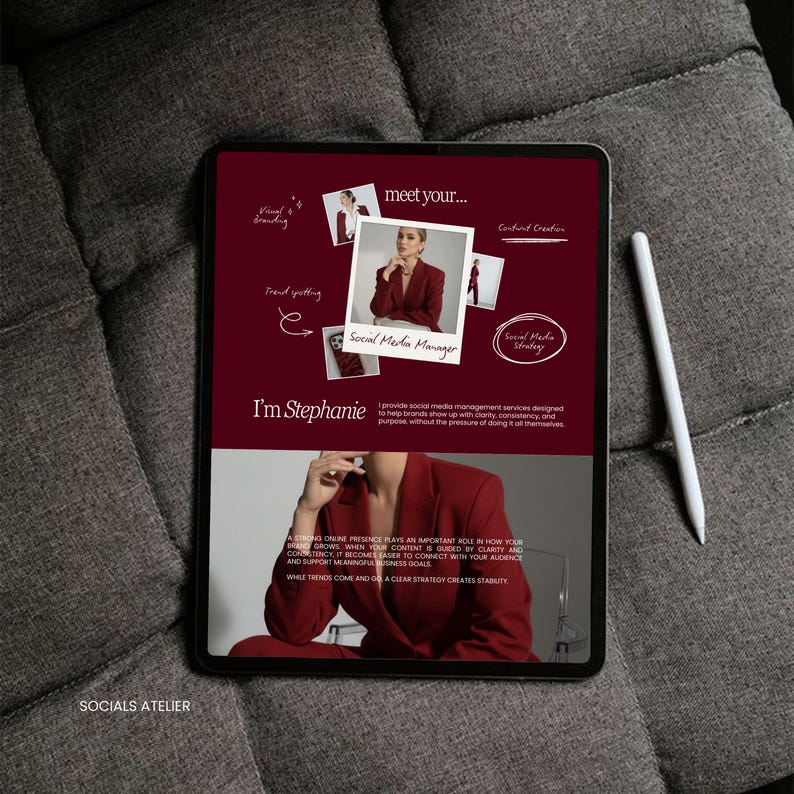 May include: A digital tablet displaying a maroon-colored graphic with the text "meet your..." and "Social Media Manager." A white stylus rests on the side. The tablet is on a gray, textured surface.