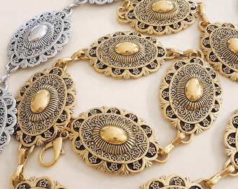 Pode incluir: Um cinto de corrente de metal dourado com medalhões ovais repetidos com padrões de estrelas em relevo e um centro liso, ao lado de um cinto de corrente de metal prateado com medalhões idênticos, ambos conectados por pequenos elos circulares.
