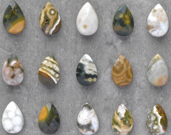 May include: Fifteen teardrop-shaped gemstones are arranged on a grey, textured surface. The stones display a variety of colours and patterns, including white, yellow, green, brown, and black. These gemstones are likely intended for jewellery making.