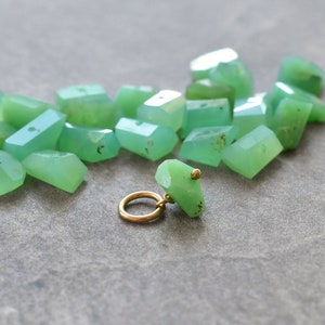 May include: A pile of green gemstone beads with a gold metal bead charm. The beads are faceted and have a translucent appearance.