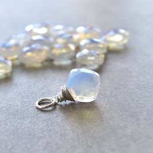 May include: A white opal gemstone pendant with a silver wire wrap. The pendant is surrounded by a scattering of smaller white opal gemstones.