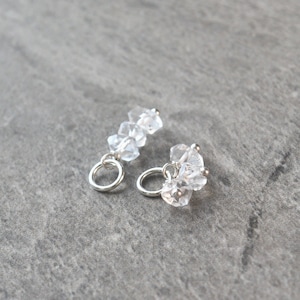 May include: A pair of silver earrings with clear crystal stones. Each earring has a small silver hoop and a cluster of clear crystals.