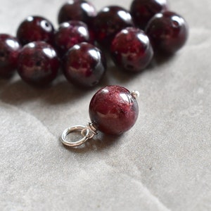 May include: A group of deep red gemstone beads, some of which are strung on a silver chain. The beads are round and smooth, and they have a slightly iridescent sheen.