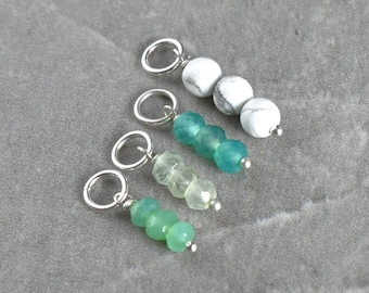 May include: Four silver charms with different coloured gemstone beads. The charms are made with three beads each. The beads are green, white, and a gradient of green. The charms are on a grey surface. Listing is for one finished charm.
