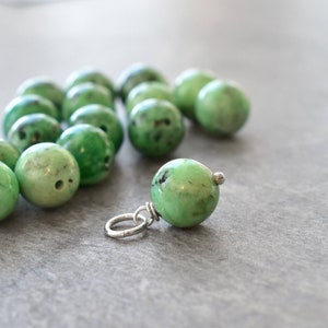 May include: A close-up of a green gemstone pendant with a silver bail. The pendant is surrounded by a group of smaller green gemstones.