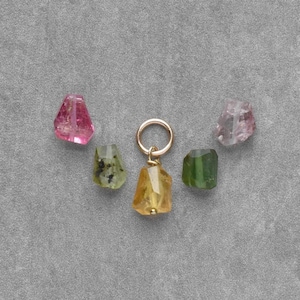 May include: A collection of colorful, raw gemstone charms. The charms include pink, green, and yellow stones, with a gold-colored ring. The stones are irregularly shaped and appear to be natural. The text in the image says "Listing for 1 finished charm."