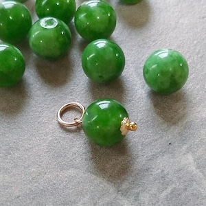 May include: A collection of green jade beads, some of which are strung together on a gold chain. The beads are various sizes and shapes, and some have a mottled appearance.