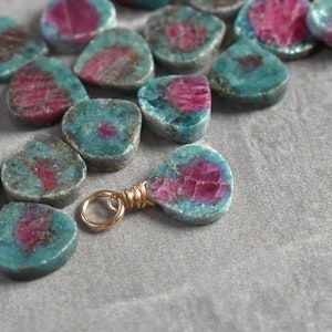 May include: A close-up of a collection of teal and pink gemstone charms. The charms are in the shape of a teardrop and have a gold jump ring attached. Listing for 1 finished charm. Stone randomly selected. Enlarged to show detail. See listing/photos for more information.