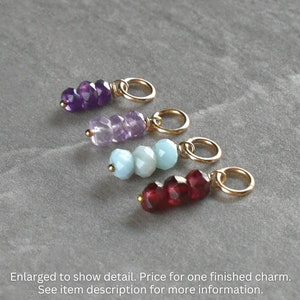 May include: Four gemstone charms with gold jump rings. The charms are made with amethyst, aquamarine, and garnet beads.