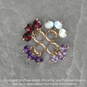 May include: Four gold charm pendants with different colored gemstones. The charms feature clusters of red garnet, blue aquamarine, and purple amethyst gemstones.