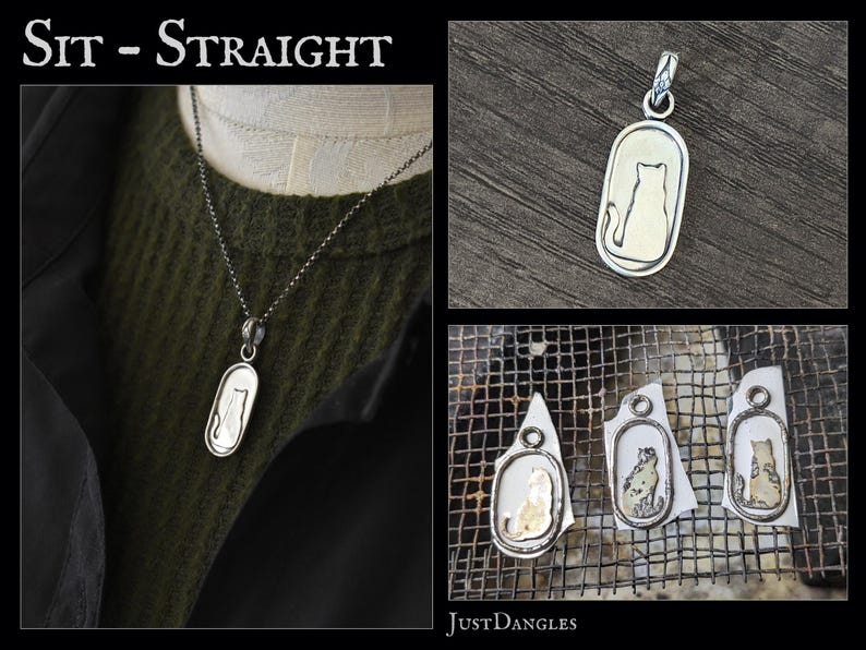 May include: A silver pendant necklace featuring a cat silhouette within an oval frame. The pendant hangs from a delicate chain. The image also shows the pendant on a dark green sweater and some work in progress.