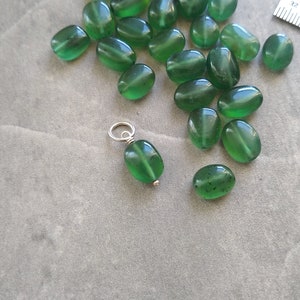 May include: A collection of green oval-shaped beads with a silver charm attached to one of the beads.