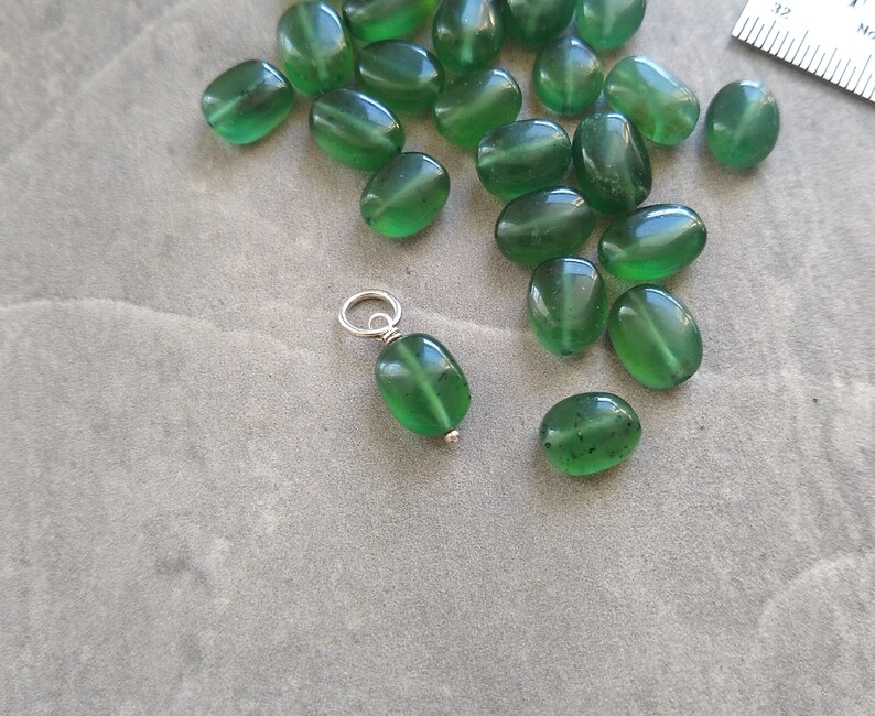 May include: A collection of green oval-shaped beads with a silver charm attached to one of the beads.