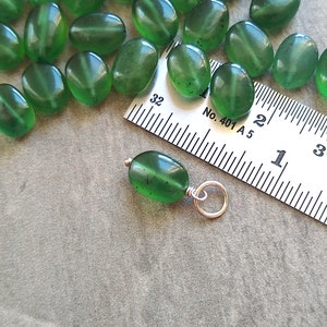 May include: A close-up of a green gemstone pendant with a silver bail. The pendant is about 1 inch long and is sitting on a ruler. The ruler is marked with inches and centimeters. The pendant is a popular choice for jewelry making.