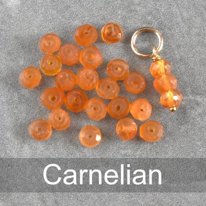 K&ouml;nnte beinhalten: Eine Sammlung von Karneolperlen in verschiedenen Oranget&ouml;nen, mit einem goldenen Anh&auml;nger an einer Schnur. Die Perlen sind facettiert und haben eine polierte Oberfl&auml;che.