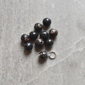 May include: A collection of black and white speckled beads with a silver jump ring.