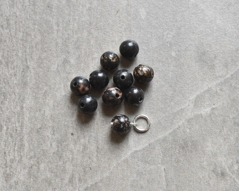May include: A collection of black and white speckled beads with a silver jump ring.