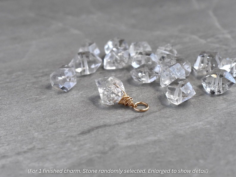 K&ouml;nnte beinhalten: Ein klarer Quarz-Anh&auml;nger mit goldfarbenem Draht und einem kleinen goldenen Ring. Mehrere andere klare Quarzkristalle sind um den Anh&auml;nger auf einer grauen Oberfl&auml;che verstreut. Der Text im Bild lautet: "(F&uuml;r 1 fertigen Anh&auml;nger. Stein zuf&auml;llig ausgew&auml;hlt. Vergr&ouml;&szlig;ert, um Details zu zeigen)".