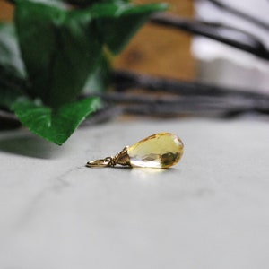Puede incluir: Un colgante de piedra preciosa amarilla en forma de l&aacute;grima con un envoltorio de alambre dorado.