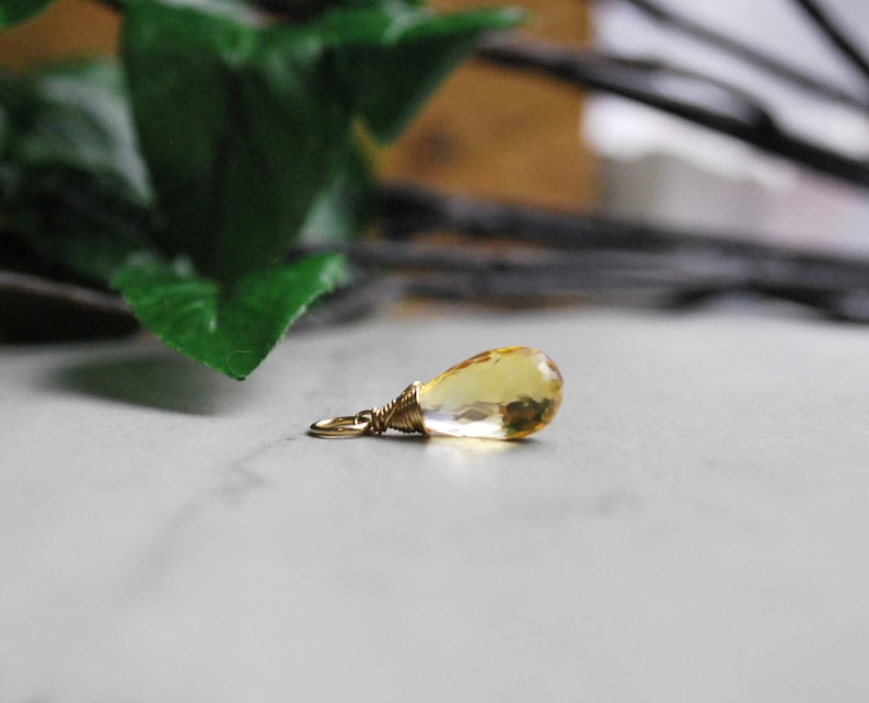 Puede incluir: Un colgante de piedra preciosa amarilla en forma de l&aacute;grima con un envoltorio de alambre dorado.