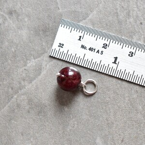 May include: A dark red wooden bead with a silver loop attached. The bead is about 1 inch in diameter.