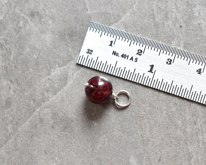 May include: A dark red wooden bead with a silver loop attached. The bead is about 1 inch in diameter.