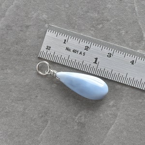 May include: A light blue teardrop-shaped pendant made of opal, approximately 1 inch long, with a silver wire wrap and a silver jump ring.