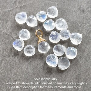 Puede incluir: Un amuleto envuelto en alambre dorado con un colgante de piedra lunar transparente e iridiscente. El amuleto est&aacute; rodeado de una dispersi&oacute;n de piedras lunares sueltas.