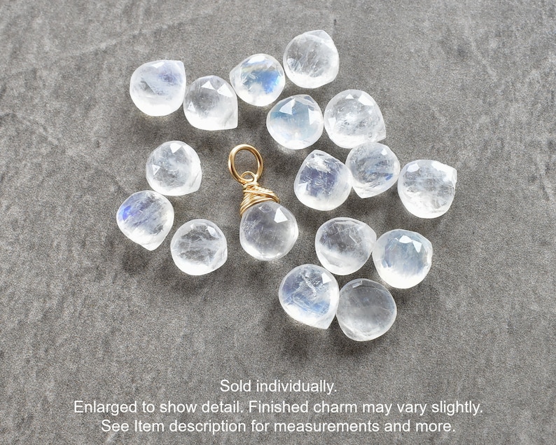 Puede incluir: Un amuleto envuelto en alambre dorado con un colgante de piedra lunar transparente e iridiscente. El amuleto est&aacute; rodeado de una dispersi&oacute;n de piedras lunares sueltas.