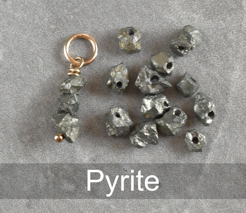 K&ouml;nnte beinhalten: Eine Sammlung roher Pyrit-Steine, von denen einige auf einer goldenen Kette mit einer kleinen Schlaufe oben aufgef&auml;delt sind. Die Steine sind in verschiedenen Graut&ouml;nen gehalten und haben eine raue, nat&uuml;rliche Textur. Das Wort "Pyrite" ist in wei&szlig;er Schrift unter den Steinen geschrieben.
