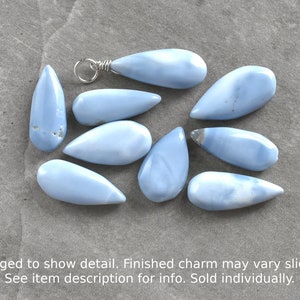 May include: Ten light blue teardrop-shaped opal stones with silver wire loops. The stones are arranged on a gray surface.