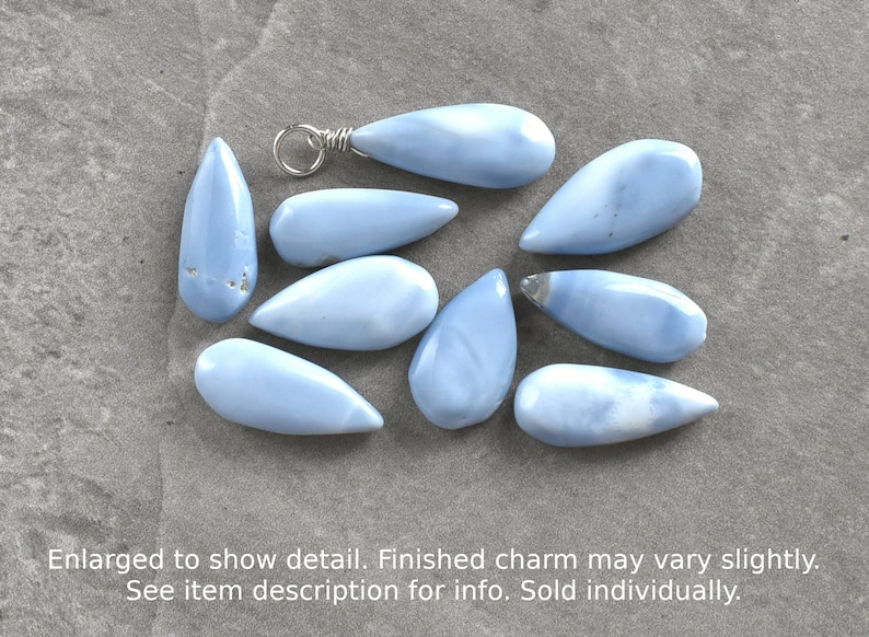 May include: Ten light blue teardrop-shaped opal stones with silver wire loops. The stones are arranged on a gray surface.
