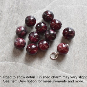 May include: A close-up of a group of dark red gemstone beads, some of which are strung on a silver chain. The beads are round and smooth, and they have a deep, rich color.
