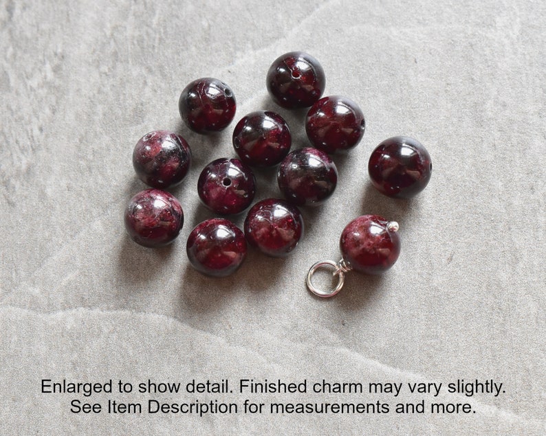 May include: A close-up of a group of dark red gemstone beads, some of which are strung on a silver chain. The beads are round and smooth, and they have a deep, rich color.