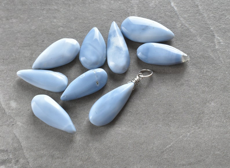 May include: A collection of ten teardrop-shaped blue opal stones, some with a silver wire loop for hanging.