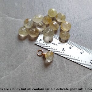 May include: A close-up of 13 cloudy, translucent, faceted, golden rutile quartz stones, ranging in size from 1/2 inch to 3/4 inch, with visible gold rutile needles. A ruler is included for scale.  The text on the ruler reads "No. 401 A 5".