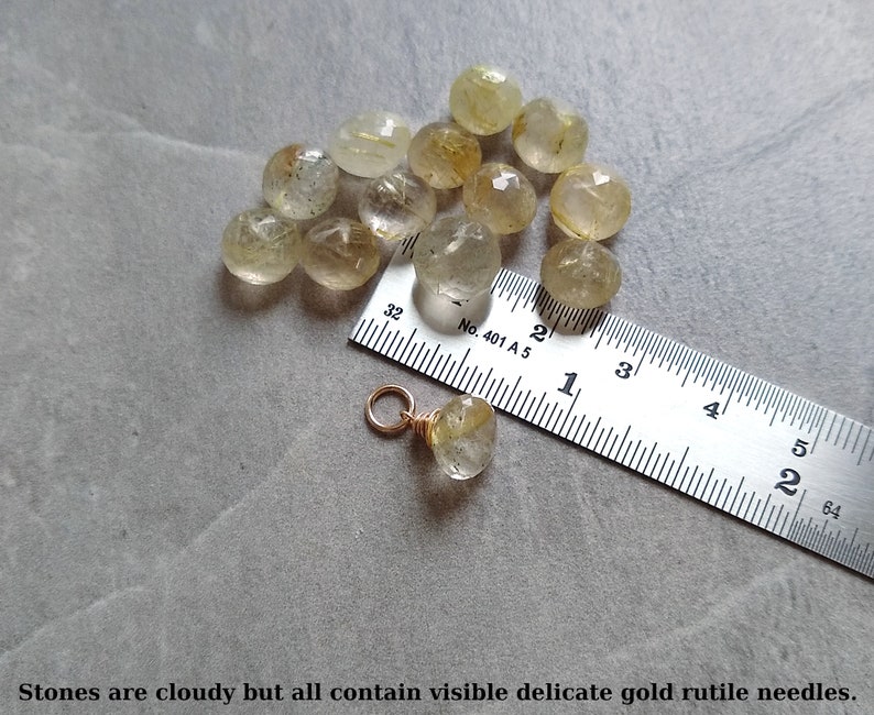 May include: A close-up of 13 cloudy, translucent, faceted, golden rutile quartz stones, ranging in size from 1/2 inch to 3/4 inch, with visible gold rutile needles. A ruler is included for scale.  The text on the ruler reads "No. 401 A 5".