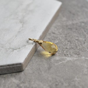 Puede incluir: Un colgante de piedra preciosa amarilla en forma de l&aacute;grima con un envoltorio de alambre dorado.