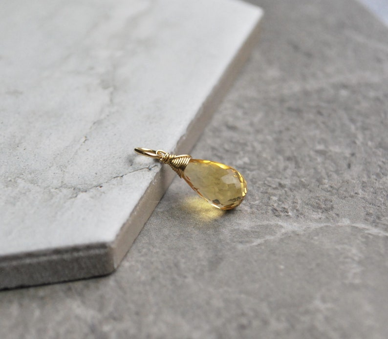 Puede incluir: Un colgante de piedra preciosa amarilla en forma de l&aacute;grima con un envoltorio de alambre dorado.
