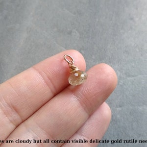 May include: A small, cloudy, golden rutile quartz gemstone pendant wrapped in gold wire.