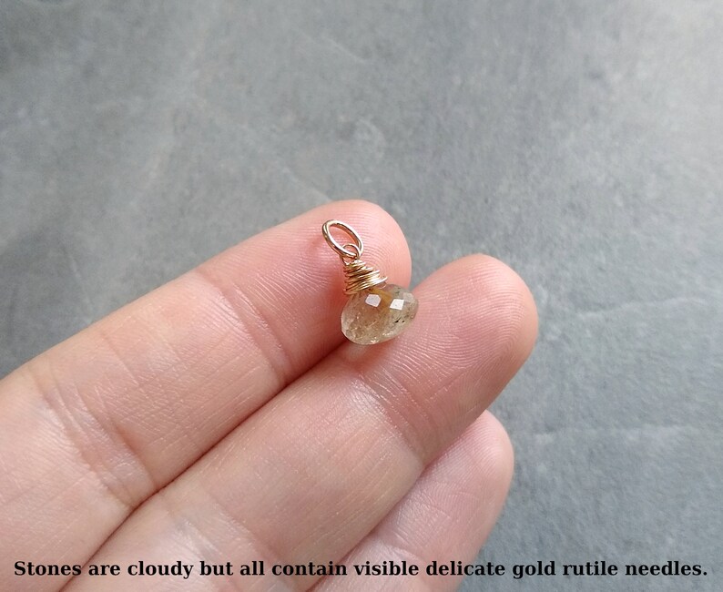 May include: A small, cloudy, golden rutile quartz gemstone pendant wrapped in gold wire.