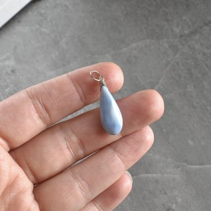 May include: A teardrop-shaped pendant made of blue opal with a silver wire wrap. The pendant is hanging from a silver chain.